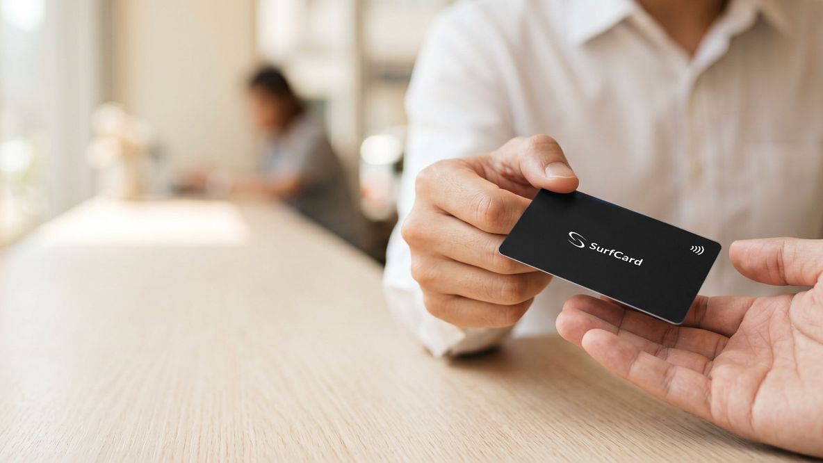 A matte black SurfCard passed from one hand to another across a cafe table