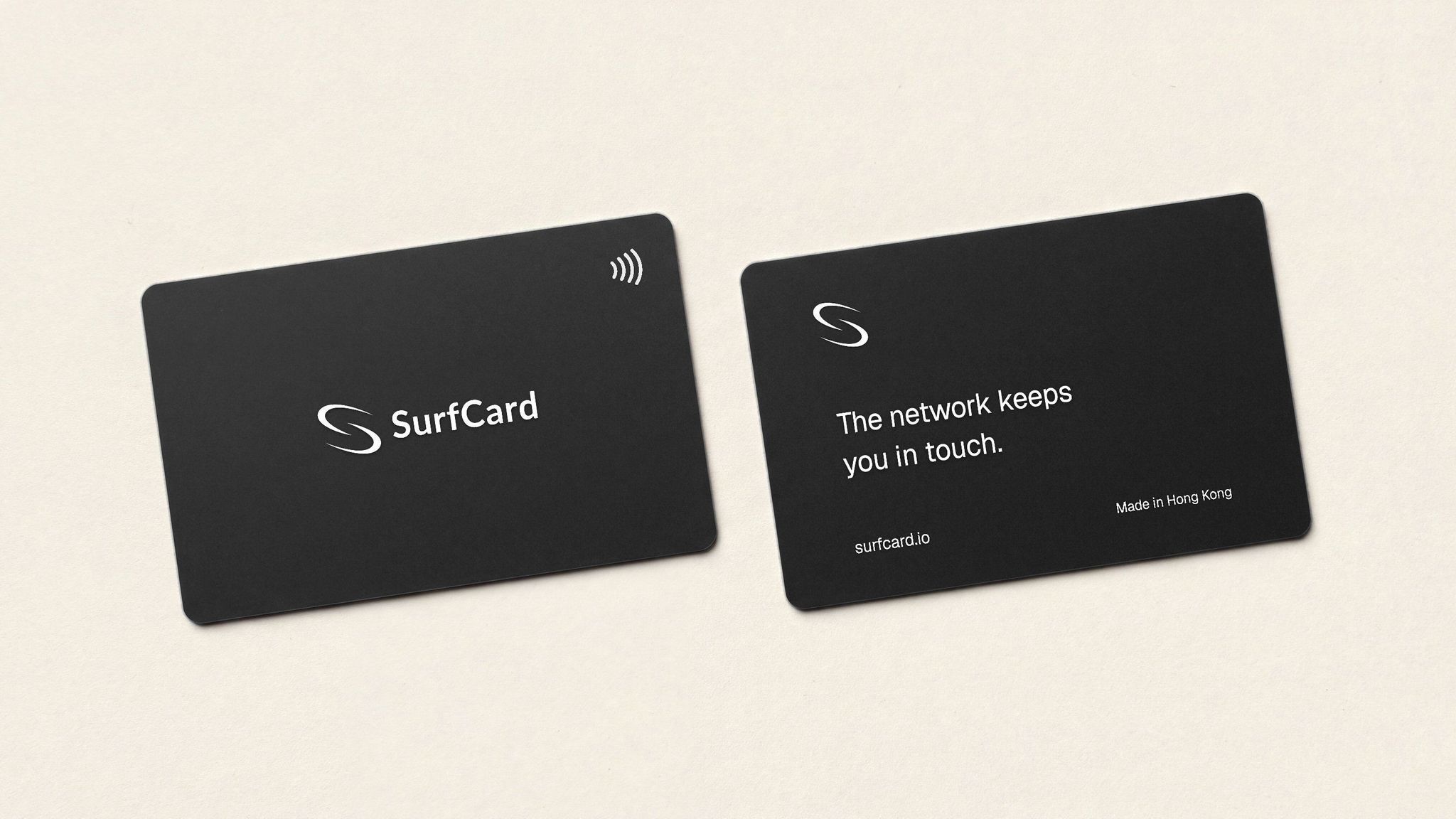 Two SurfCard Classics side by side on a pale studio surface — one face up with the SurfCard mark and the contactless indicator, the other showing its back, printed with the square SurfCard mark, the line “The network keeps you in touch.”, surfcard.io and “Made in Hong Kong”