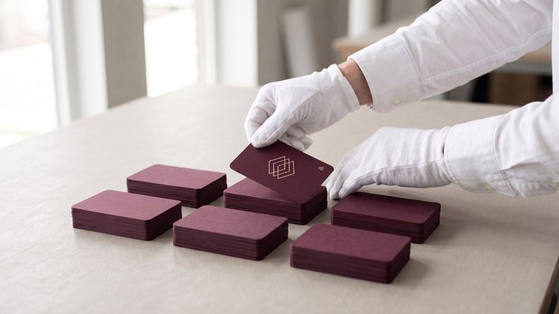 Gloved hands placing a burgundy company card onto one of six freshly made stacks