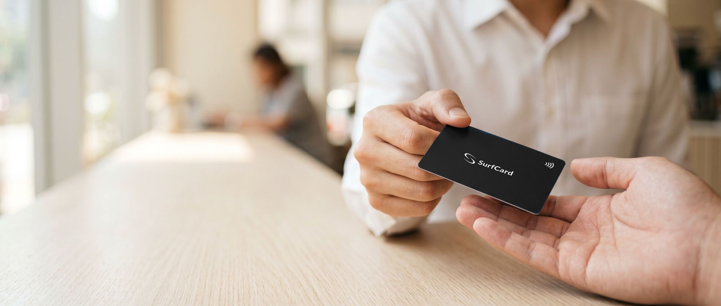 A matte black SurfCard passed from one hand to another across a cafe table